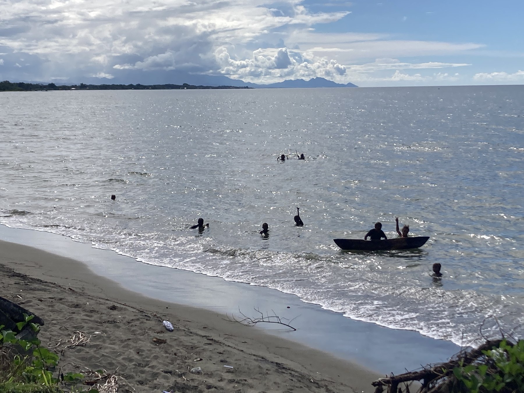 People swimming and paddling along a Solomon Islands shoreline